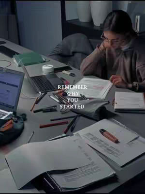A dimly lit study scene with a woman wearing glasses focused on a book. Scattered papers, pens, a laptop, and a pencil case are on the desk. A text overlay reads, 'REMEMBER WHY YOU STARTED.' The color palette is muted with cool tones.