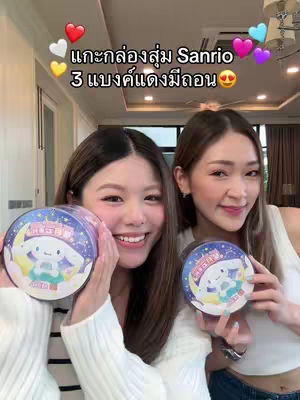 Two smiling women hold up Sanrio blind box containers. The image is well-lit, with a soft focus. Above them are colorful heart and star stickers.