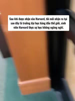 The image presents a blurred interior shot featuring a tall, brown, wooden structure on the left, possibly a pillar or a wall. The background is slightly out of focus, with a dark tone suggesting a shadowy or indoor setting. In the center of the frame, there is a white rectangular text overlay, containing Vietnamese text. The overall composition is simplistic, focusing on the texture and the contrast between the elements present.