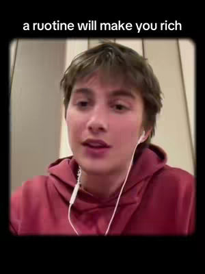 A young person with light skin and brown hair is centered in a vertical video frame. The person is wearing a red hoodie and white earbuds are visible. The background appears slightly blurred, suggesting an indoor setting. Above the person, the text overlay reads, "a ruotine will make you rich."