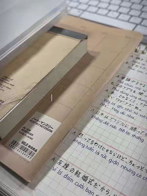 An overhead shot of a study setup. A notebook and an open book with handwritten notes are visible. A keyboard is partially visible in the background.