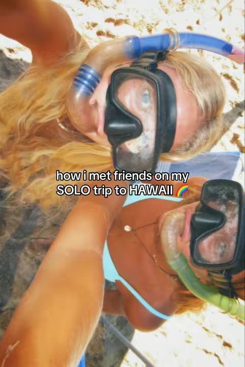 The image captures a woman snorkeling in Hawaii, wearing a snorkel mask and blue bikini top. The background shows a sandy beach. Text overlayed on the image reads, 'how i met friends on my SOLO trip to HAWAII' with a rainbow graphic.