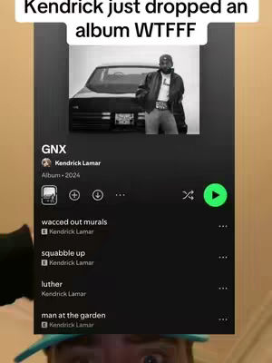 A vertical video screenshot featuring a Spotify interface displaying an album by Kendrick Lamar. The background is tinted a brown-beige color. At the top, overlaid text reads "Kendrick just dropped an album WTFFF". Below that, the album artwork shows Kendrick Lamar in black and white standing in front of a car. The rest of the interface lists songs from the “GNX” album, along with the play button, all presented in a black background.
