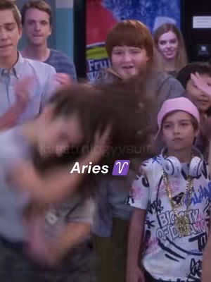 The cover image shows a group of people in a hallway setting. In the foreground, a person has their head down in motion and to the right of the frame, a young person in a pink hat looks at the camera. The words 'Aries ♈' are overlaid on image.