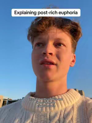 A selfie-style shot of a young man against a clear blue sky. He is wearing a white sweater and appears to be speaking. Text overlays at the top and bottom of the screen provide additional context.