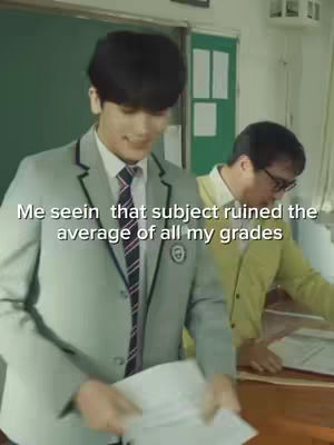 A young man in a school uniform is looking down at a paper in his hands with a slight smile, while another man is standing in the background, near a blackboard. The text overlay expresses a relatable student sentiment.