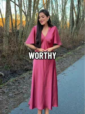 A woman in a long pink dress stands in front of trees on a path, text overlayed on the image.