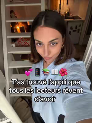 A selfie-style shot featuring a woman slightly angled towards the camera in an indoor setting. The woman is fair-skinned with brown hair, wearing a light blue collared shirt, and gold hoop earrings. At the bottom, overlaid text in white declares in French 'T'as trouvé l'appli que tous les lecteurs rêvent d'avoir.' The background is softly lit, showing a staircase, white shelves, and a peek of a kitchen.