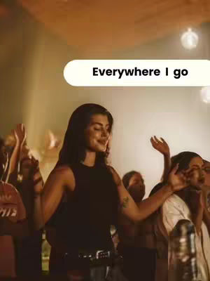The cover image shows a woman with dark hair in a musical performance setting. She is wearing a black top and is mid-gesture with her arms outstretched, presumably singing, with an intent expression. The background is blurred, but includes other people, suggesting a concert or worship service. The lighting is warm, and there's a text overlay.