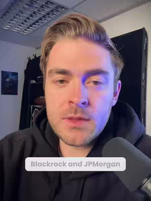 A man with light brown hair is centered in the frame, looking towards the camera. He is wearing a black hoodie. A text overlay at the bottom indicates the topic. The background is an office with a mic in the foreground.