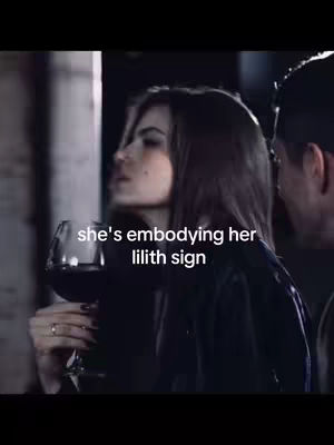 The cover image shows a woman holding a wine glass, looking towards the left side of the frame. The image has a dark and moody aesthetic. There is text overlayed with the words: 'she's embodying her lilith sign.' The background is out of focus and slightly blurry.