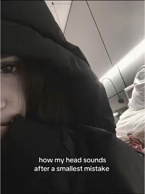 A close-up shot of a person, likely a young female, with a black hoodie. The image focuses on her face and the hood, creating a dark, somber atmosphere. The hood covers most of her head, making the background out of focus and less visible. The lighting is dim, which, combined with the hoodie, helps to create an emotional or intense mood.