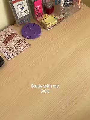 A top-down image of a wooden desk with study supplies, including a notebook, round purple coaster, pens, sticky notes, and notebooks. The text overlay reads "Study with me 5:00".