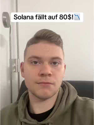 A man in a green hoodie is in the middle of the frame, with a text overlay that says 'Solana fällt auf 80$!' in a white box at the top. The background is a plain white wall. The man has short hair and is looking at the camera.