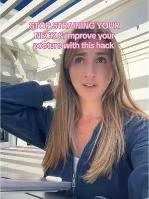 A woman with long blonde hair is centered in the frame, looking towards the viewer. She wears a dark blue zip-up jacket over a white top. The background shows a slatted overhead structure and a white wall. Text overlay reads 'STOP STRAINING YOUR NECK & improve your posture with this hack' in a pink hue.