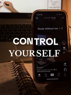 A person is holding a phone displaying a social media app with text overlays. A notebook and laptop are in the background, suggesting a study environment. The overall lighting is dim, possibly at night.