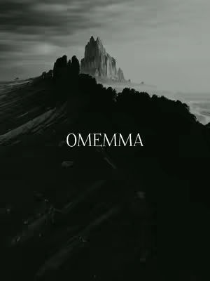 A black and white image featuring a dark, imposing landscape. The foreground is a shadowed, rugged mountain range, with a prominent, sharply pointed rock formation rising in the distance. The sky is overcast, creating a dramatic and somber atmosphere. The word 'OMEMMA' is written in a clean, white font across the lower half of the image.