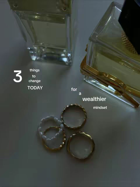 An overhead shot featuring two rectangular perfume bottles and four gold rings. The items are arranged on a light-colored surface. Text overlays are added, with the numbers and words for the hook. The lighting is soft and creates subtle shadows.