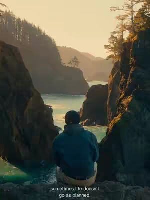 The image shows a scenic landscape with a body of water surrounded by mountains. A person is seen from the back, sitting on a rock, looking out towards the vista. The sky is bright with the sun setting.
