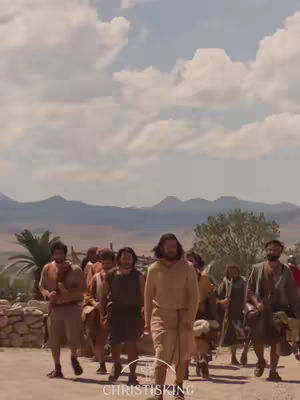 A crowd of people walking in a procession on a dirt path, with a landscape of rolling hills and a cloudy sky in the background. The people are dressed in ancient-style clothing. The central figure, presumably Jesus, is in the center of the crowd and the logo of christisking.com is featured in the image.