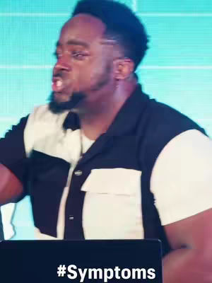 The cover image captures a close-up of a man in a black and white collared shirt, appearing to be speaking passionately. His expression is intense, with his mouth open and eyes wide. The background suggests a stage or studio setting, with a grid-like pattern creating a sense of depth. At the bottom of the image, the text '#Symptoms' is prominently displayed.