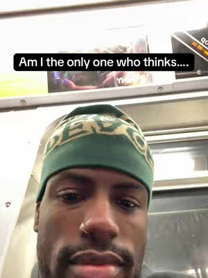 A close-up shot of a Black man inside a subway car. He's wearing a green and tan patterned beanie hat, and his facial expression is neutral with a slight downward gaze. The background includes a glimpse of what seems to be a poster. A text overlay in a black rectangle says, "Am I the only one who thinks...."