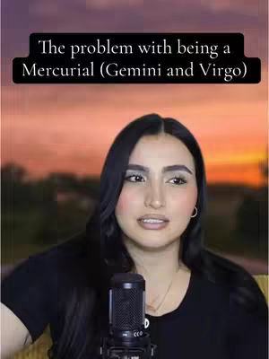 A woman with long black hair is centered in the frame, a microphone positioned in front of her. She gazes toward the left. Above her, a black box with white text provides context. The backdrop is a soft gradient of colors, suggesting a sunset or sunrise.