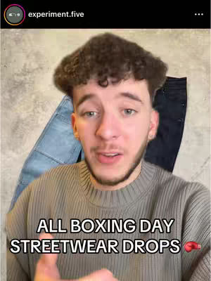 A young man with a beard and short curly hair is centered in the frame, smiling slightly, against a light background with items in the background that appear to be jeans. Text overlayed on the image reads: 'All Boxing Day Streetwear Drops'. The text is in a bold white font, and a boxing glove emoji is at the lower right.