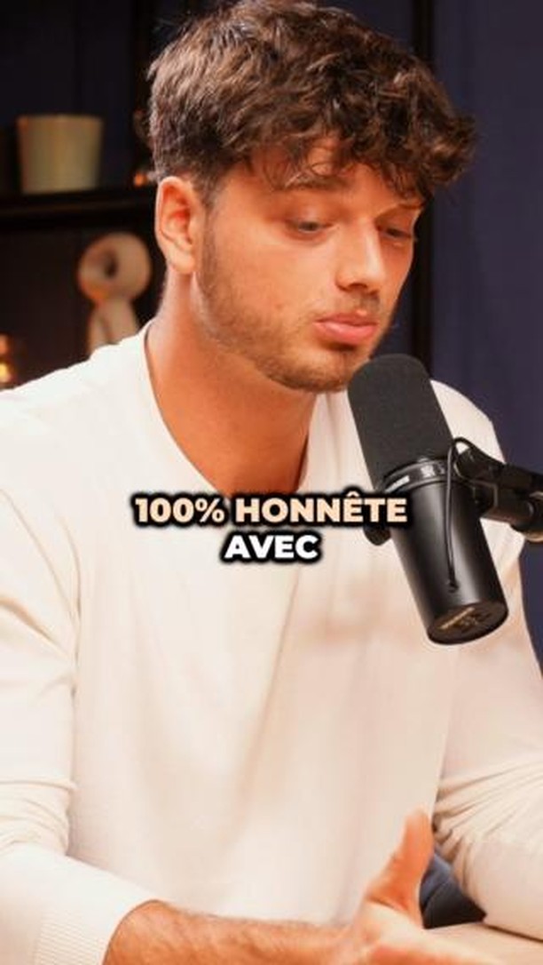 The cover image shows a man, presumably the creator, angled slightly towards the camera. He's wearing a white shirt and is holding a black microphone in front of his mouth. The background is dark and blurred, with the upper portion of a dark wooden desk partially visible. Overlayed on the image is the text "100% HONNÊTE AVEC" in a bold, white font.