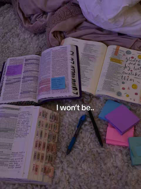 An overhead shot shows several open Bibles with handwritten notes, tabs, and sticky notes on a textured carpet. Pens and a stack of sticky notes are scattered around the Bibles. The background consists of wrinkled fabric.
