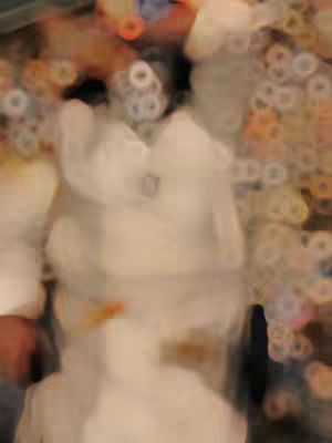 The image appears to be blurred and out of focus, making it difficult to discern specific details. The background seems to have bokeh-like circular shapes, suggesting lights or a blurred environment. The main object of focus is difficult to identify due to the blur, but it seems to be a person with what appears to be a light-colored shirt.