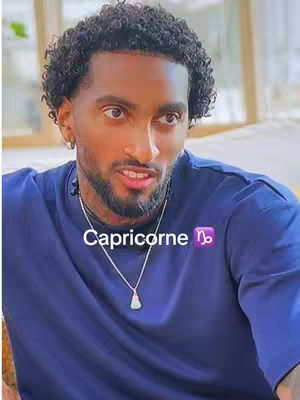 The cover image is a close-up shot of a dark-skinned man with short, curly black hair and a groomed beard. He is wearing a dark blue t-shirt and a silver necklace. Overlayed on the image is the text "Capricorne" in white, with the Capricorn zodiac symbol next to it. The background appears to be a softly lit indoor setting.