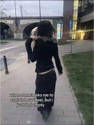 The cover image depicts a person walking away from the camera on a city sidewalk. The person is dressed in all black clothing and is wearing a hat. Text overlayed on the image reads "when some1 asks me to explain how i feel, but i just feel empty."
