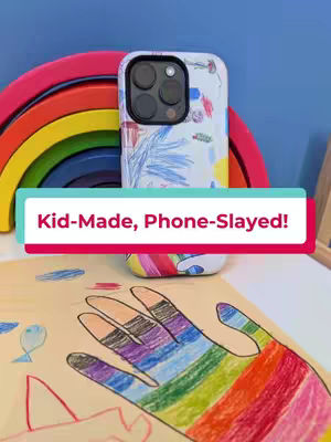 The cover image features a phone case with a drawing of a hand, colored with rainbow hues, resting on a piece of paper. Above the paper, a rainbow-colored arch and a phone case with a design are positioned against a blue background. Text that reads 'Kid-Made, Phone-Slayed!' is on top of the case.