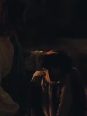 The cover image shows a dark scene with two figures. The background appears dim, possibly lit by a small fire. One figure is partially visible on the left, and another in the center, with their head bowed. Colors are subdued dominated by blacks, browns and yellows due to the firelight. The overall composition is dark and mysterious.