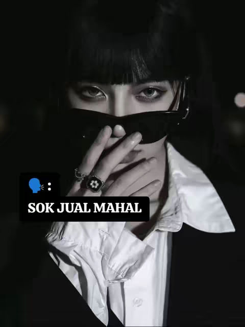 A close-up shot focusing on the upper part of a person's face, mainly their eyes and the lower area covered by sunglasses. The person is wearing dark sunglasses and is holding a finger up to their mouth, suggesting a shushing gesture. The background is dark, and there is a text overlay in the bottom foreground. The shot is in black and white.