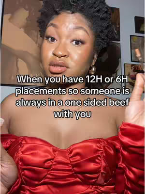 A medium shot features a Black woman looking directly at the camera with a serious expression. She has styled short, dark, curly hair, and is wearing a strapless, bright red dress. The lighting appears to be soft and diffused, and the background is blurred, suggesting a domestic setting.