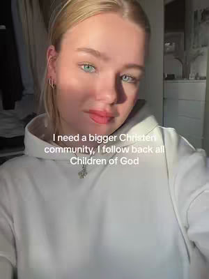 A young woman with blonde hair and green eyes is taking a selfie. She is wearing a white hoodie and a necklace with a small pendant. Text overlays the image with a call to action.