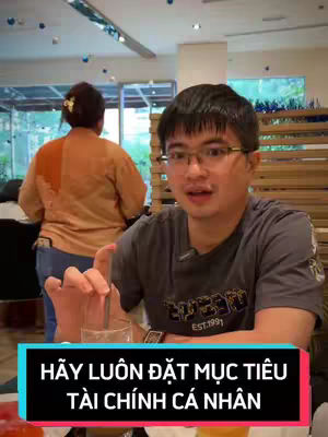 A man in glasses sits in a cafe setting, with a person blurred in the background. The man is holding a glass with a drink. The text overlay is displayed in a rectangular box.