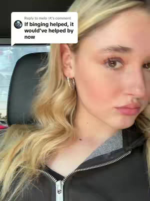 A close-up shot of a woman, slightly angled to the right. She has long, wavy, blonde hair and is wearing a black zip-up jacket. The background is blurred.