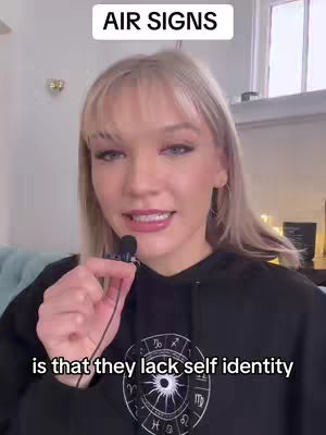 A woman with blonde hair and a black hoodie is speaking into a microphone. Above her head, the text 'AIR SIGNS' is displayed. In the bottom of the frame, text floats over the image.