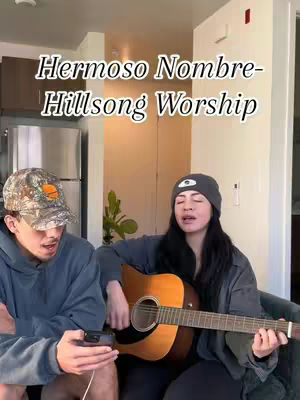 The cover image shows a man and a woman, presumably a couple, in an apartment. The woman is singing and playing an acoustic guitar while the man is sitting next to her holding a phone. Text overlayed with the name of the song they are performing.