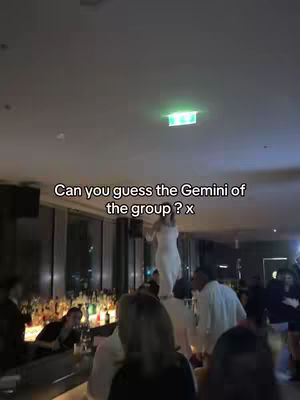 A woman stands on the shoulders of other people in a crowded bar, with the caption 'Can you guess the Gemini of the group ? x' at the bottom.