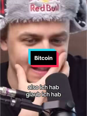 A man wearing a gray Red Bull hat is featured, with a framed graphic of a bitcoin and text overlay with german sentences, the man covers his mouth with a hand and a microphone in the foreground.