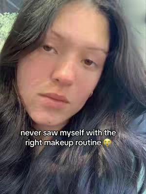 A close-up shot of a person with dark hair, slightly out of focus. The person has fair skin and is looking slightly downwards with a pensive expression. Text overlayed at the bottom states: "never saw myself with the right makeup routine" with a smiling emoji.
