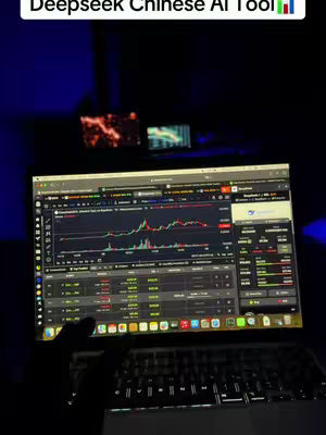 A laptop displaying a trading interface is illuminated in a dim environment, with a hand partially visible on the keyboard. Above the screen, two smaller monitors are faintly lit, possibly displaying additional information or visuals. The overall composition is dark, focusing attention on the laptop screen's data.