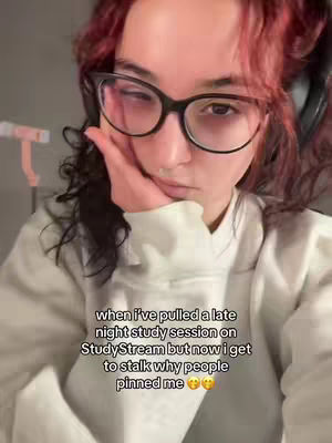 A selfie-style shot featuring a young woman with red-tinted hair and glasses. She's holding her face with one hand, wearing a white hoodie, and there's overlay text at the bottom detailing a late-night studying session experience.