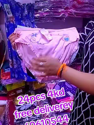 A woman's hand holds up a pair of light pink women's underwear. The underwear features a ruffle around the top and a decorated bow. The background is blurred but filled with shelves containing various items, likely within a store. Overlay text provides pricing and contact information.