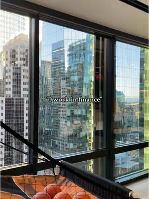 A view of a modern city skyline is seen through large windows. Text overlayed in the image says: "I work in finance". A basketball hoop filled with basketballs sits in front of the window
