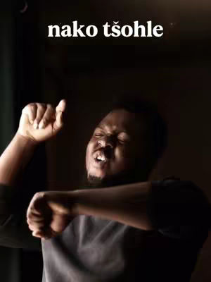The image features a dark-skinned man with an open mouth and raised arms, portraying an emotional expression. The background is dark, and the text overlayed at the top says "nako tšohle".